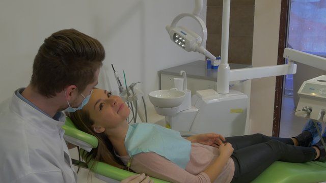 Woman Patient is Smiling Talking to Dantist Looking at Mirror Dantist in Mask is Listening Talking Examining a Teeth of a Patient Dental Treatment Room