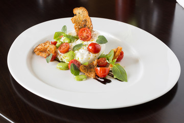 Delicious tomato and mozzarella cheese salad caprese, served on a white plate, with basil, croutons and balsamic vinegar.