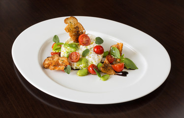 Delicious tomato and mozzarella cheese salad caprese, served on a white plate, with basil, croutons and balsamic vinegar.