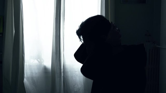 Silhouette of Desperate Sad Man in The Dark. Backlit silhouette of a desperate man making a prayer at home in the dark