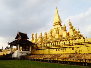 Golden temple in Laos under cloudy sky.