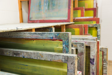 Silk screen printing screens stored in a wooden rack ready for printing.