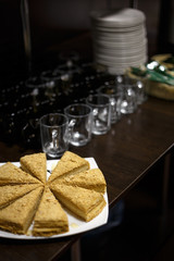 Sliced cake on white plate next to emty cups and pile of plates on wooden bar counter