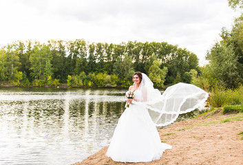 Fototapeta na wymiar bride in a white dress with wedding bouquet at the lake