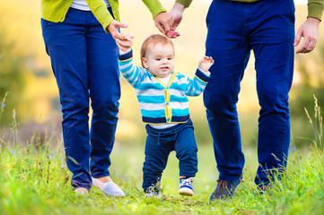 Parents holding hands of their son making first steps