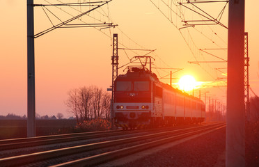 Naklejka na ściany i meble Passenger train on railway at sunset