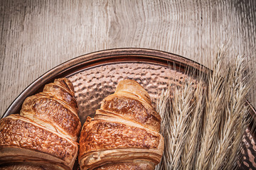 Composition of wheat rye ears croissants copper tray on wooden b