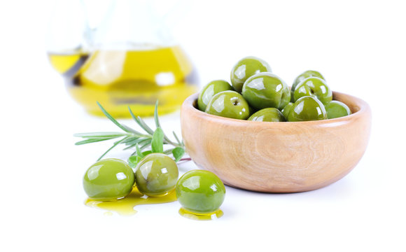 Green olives in wooden bowl with rosemary and extra virgin olive oil isolated on white background, closeup.