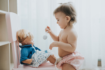 Cute baby girl playing in a white room in the morning with toys