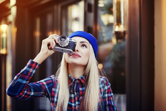 Stylish happy smiling hipster girl with old retro vintage camera. Lady looking up and taking picture. City lifestyle. Copy space, free text. Toned