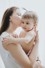 Beautiful mother portrait playing with her cute little girl in a white room in the morning