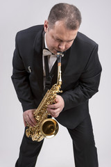 Naklejka premium Caucasian Man in Suite Playing the Saxophone. Posing Against White