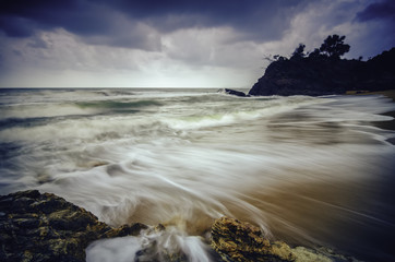 stunning white wave flow hitting the sandy beach with dark cloud. classic tone color applied.