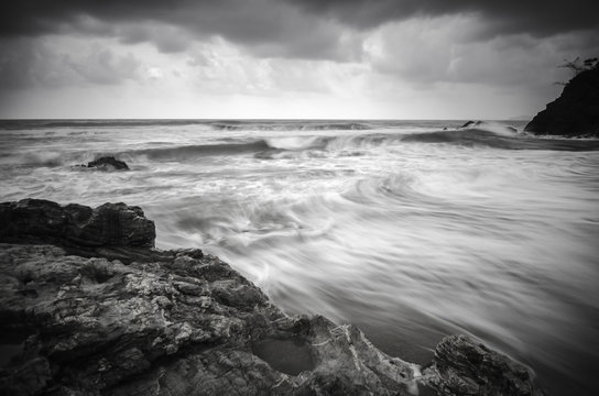 Fototapeta black and white image wave flow on the sandy and rocky beach with dark and dramatic cloud.