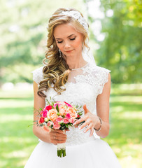 Beautiful bride outdoors in a park with wedding bouquet.