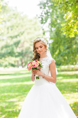 Obraz na płótnie Canvas Beautiful bride outdoors in a park with wedding bouquet.