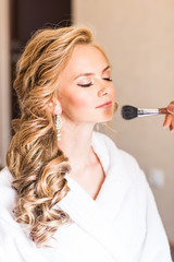 Obraz premium Wedding makeup artist making a make up for bride. Beautiful sexy model girl indoors. Beauty blonde woman with curly hair. Close-up hands near face