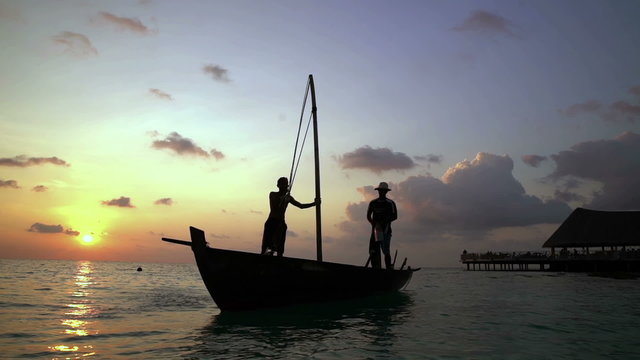 Two fishermen scooped water out of an old wooden boat at the end of a hard day at sunset in the Indian Ocean. Slow motion.