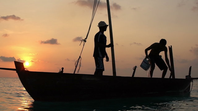 Two fishermen scooped water out of an old wooden boat at the end of a hard day at sunset in the Indian Ocean. Slow motion.