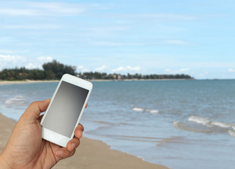 hand holding the smartphone on blurred sea background