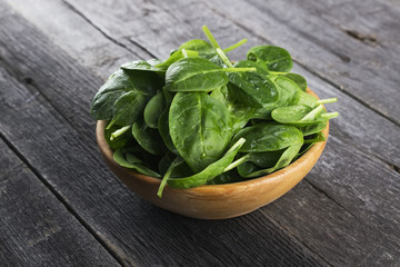Spinach leaves in bowl on dark wooden background
