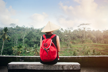 Young lady with traditional Asian hat with backpack sitting near tea plants (intentional sun glare)