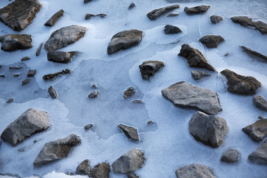 Rocks in the icy water. Stones are surrounded by thick ice due to cold day in the winter time.