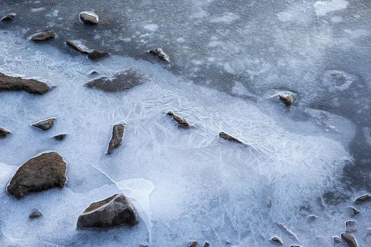 Rocks in the icy water. Stones are surrounded by thick ice due to cold day in the winter time.