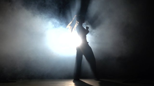 Girl with muscled body. Training martial arts. Black. Silhouette. Backlight