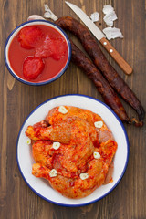 raw chicken with black pepper and knife in dish and tomato on brown wooden background