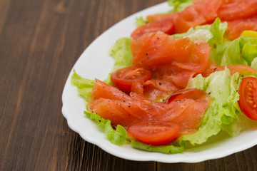 salad with smoked salmon on white dish on brown wooden background