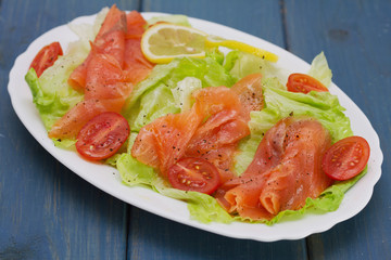 salad with smoked salmon on white dish on blue background