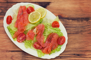 salad with smoked salmon on white dish on brown wooden background