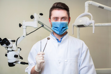 people, medicine, stomatology and healthcare concept - happy young male dentist with tools over medical office background