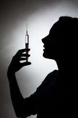 Silhouette of a girl with a syringe on a gray background.