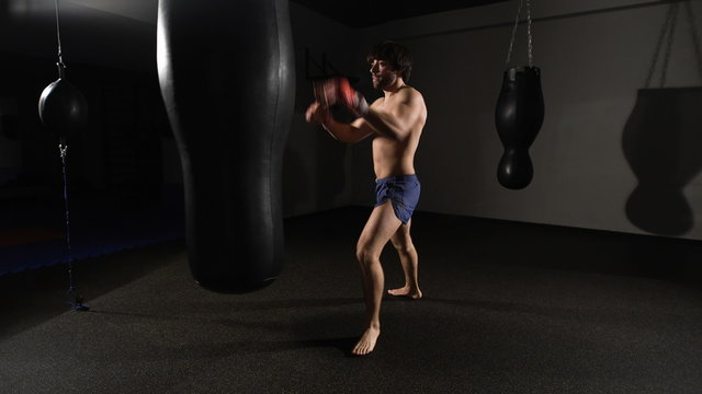fury. muscular handsome fighter giving a forceful forward kick during a practise round with a boxing bag, kickboxing.