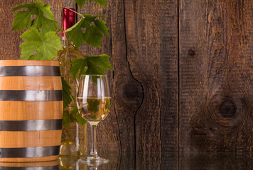 Glass of wine with barrel white bottle behind grapeleaves