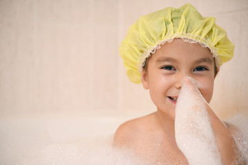 バブルバスの中で楽しむシャワーキャップをかぶった女の子、泡を自分の鼻につける。