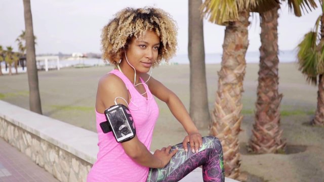 Single beautiful calm young woman in pink shirt and tights stretching her arms and side with leg on concrete wall at summer beach resort