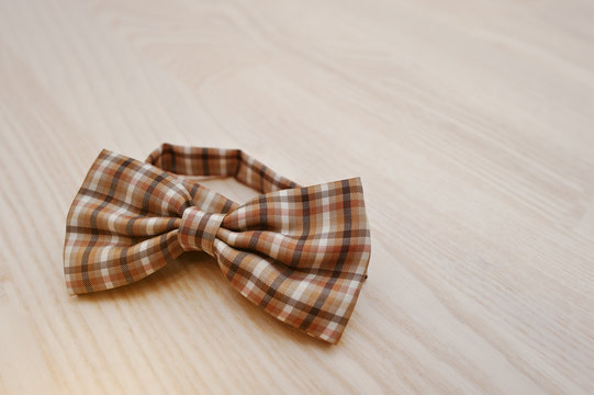 Brown checkered bow tie on light wooden background