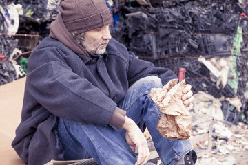 homeless man with a bottle of red wine in landfill