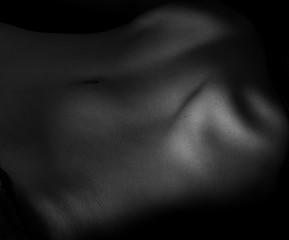 Naked belly on dark background. Black and white toning.