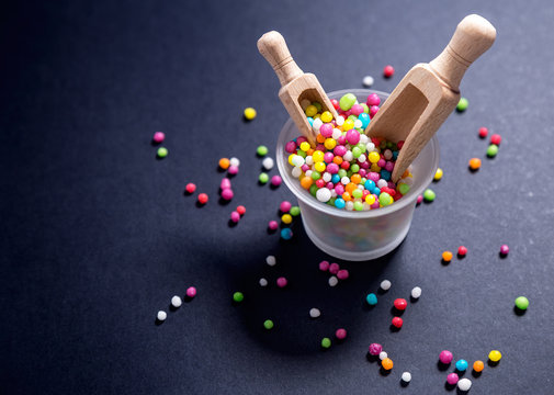 Colored candy,sugar pearls with wood scoop on black background