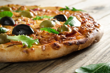 Delicious pizza with cheese and black olives on wooden table, side view.
