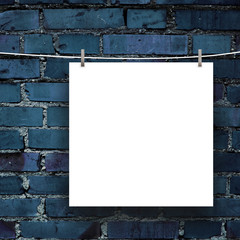 Close-up of one hanged square blank frame with pegs against dark blue brick wall background