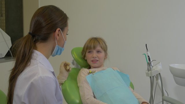 Dentist is Talking to Girl Calms the Patient Doctor in Mask is Examining a Teeth of a Patient Explains Something Dental Clinic Visit to the Dentist