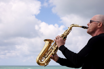 Obraz na płótnie Canvas Saxophonist playing on saxophone on blue sky background