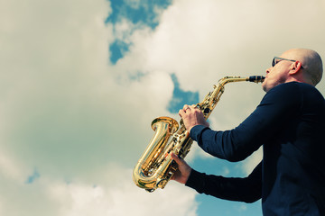 Naklejka na ściany i meble Saxophonist playing on saxophone on blue sky background