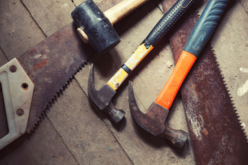 A variety of hammers and saws lays on wooden floor