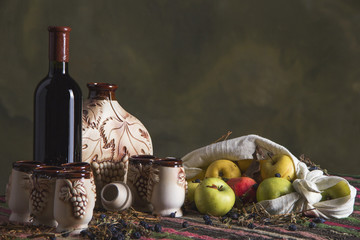 Folklore table with ethnic carpet, sweet wine, jug, glasses, apples